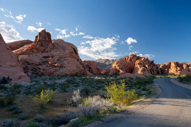 A quiet road winding past red sandstone rock formations in the desert under a deep blue sky.