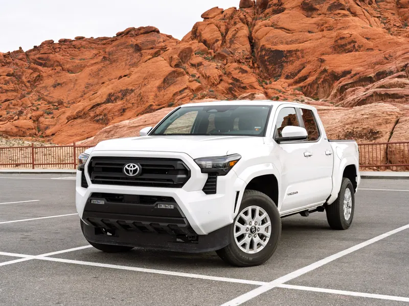 A white pickup truck parked in front of red desert rock formations.