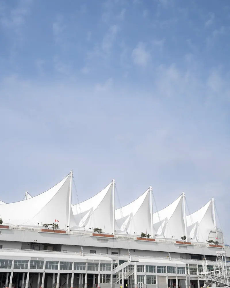 The white, sail-shaped roofline of a waterfront building against a pale blue sky.
